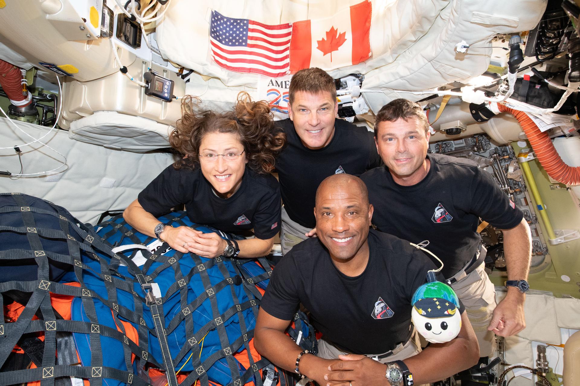 Les astronautes d'Artemis II (Christina Koch, Jeremy Hansen, Reid Wiseman et Victor Glover) posant à l'intérieur du vaisseau Integrity avec Rise, la peluche indicateur d'apesanteur en forme de Lune portant une casquette Terre.